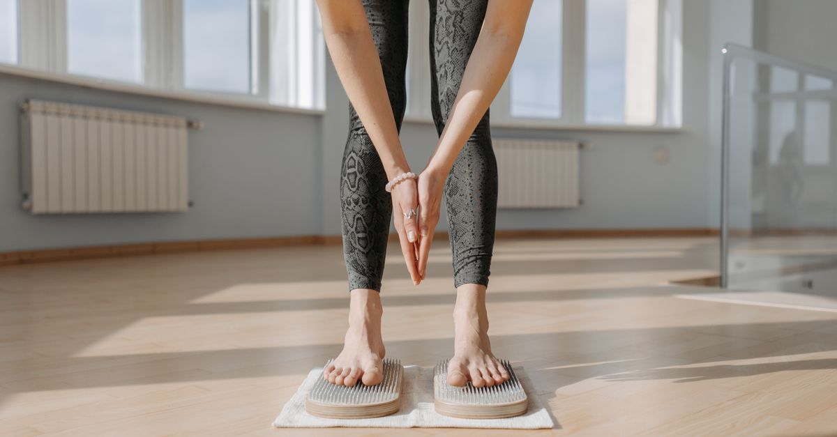 An adult woman performs yoga on a sadhu board indoors, focusing on balance and mindfulness.