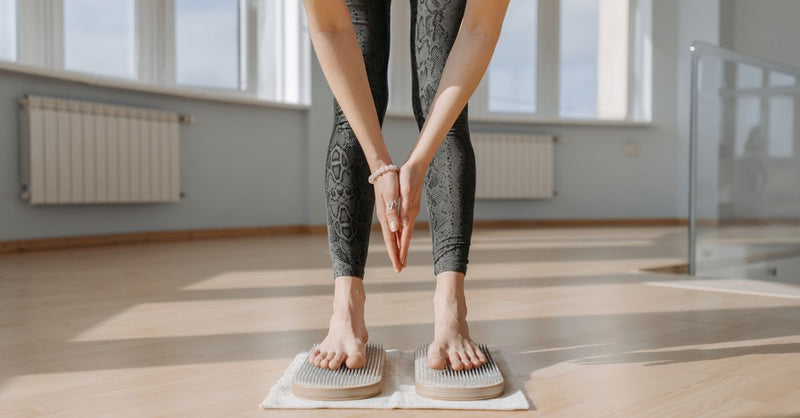 An adult woman performs yoga on a sadhu board indoors, focusing on balance and mindfulness.