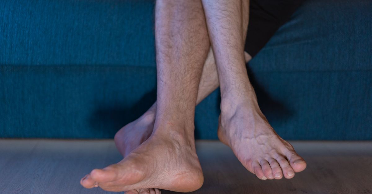 A close-up of a person's crossed legs and bare foot, relaxing inside on a couch.