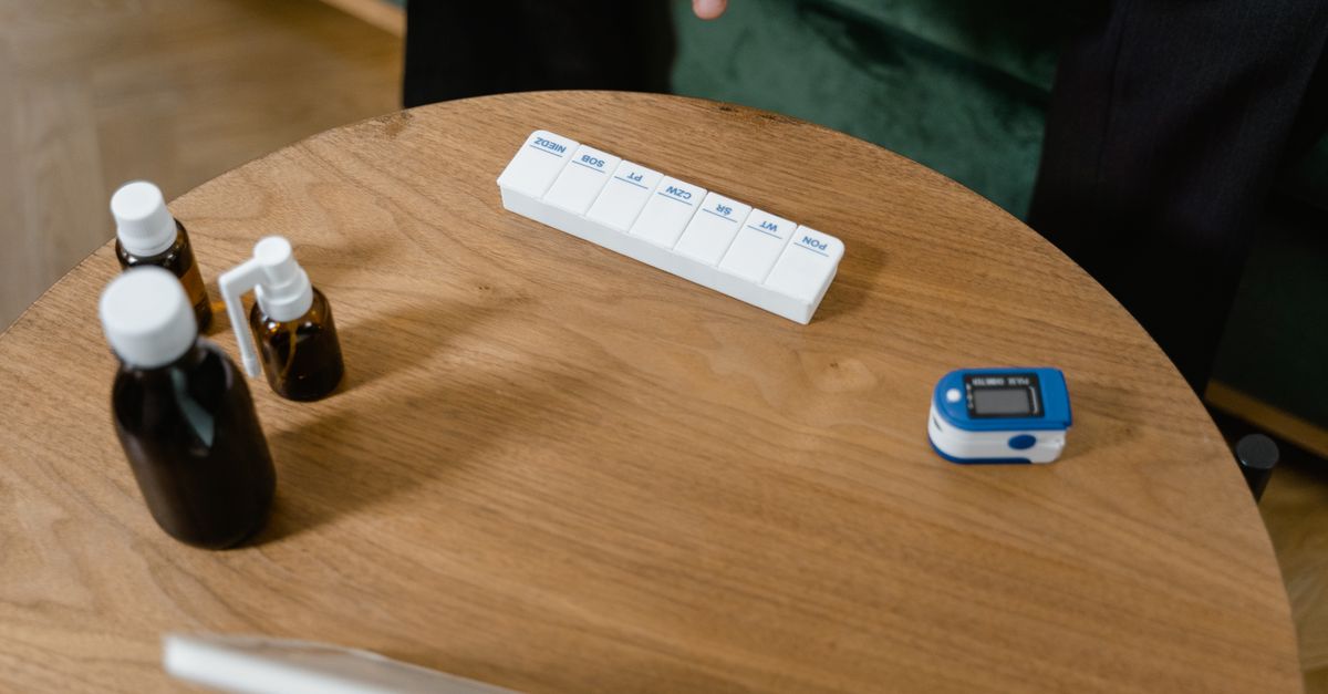 Pill organizer and medication bottles on a wooden table with a pulse oximeter.