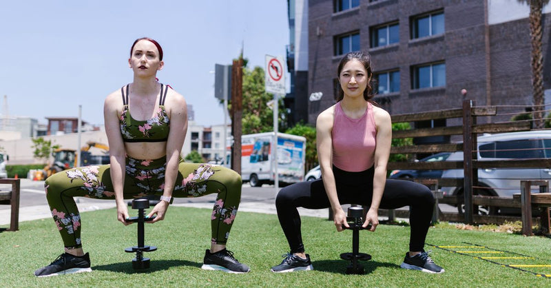 Two women exercising outdoors with weights, focusing on fitness and strength training.
