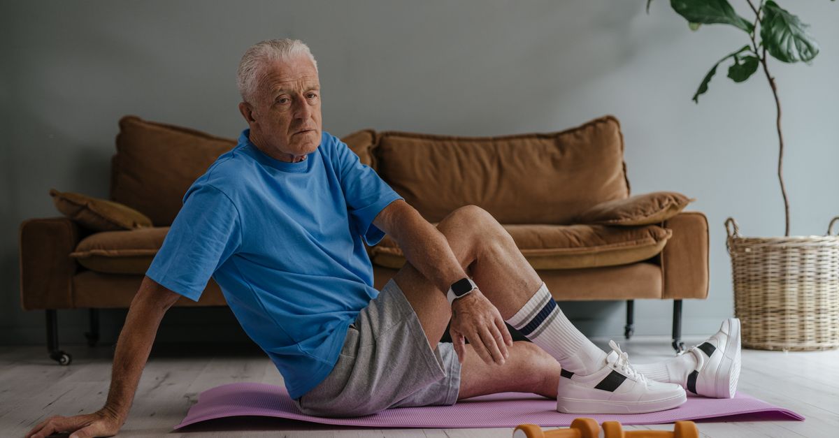Older man exercising indoors on a yoga mat with light weights.