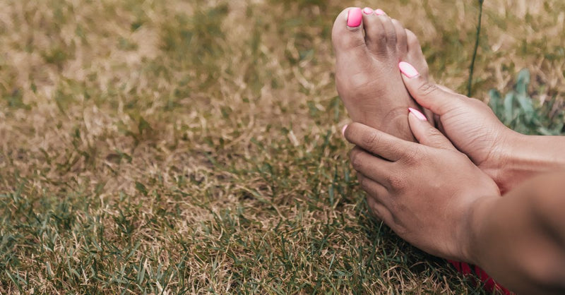 Hands holding a bare foot resting on the grass.