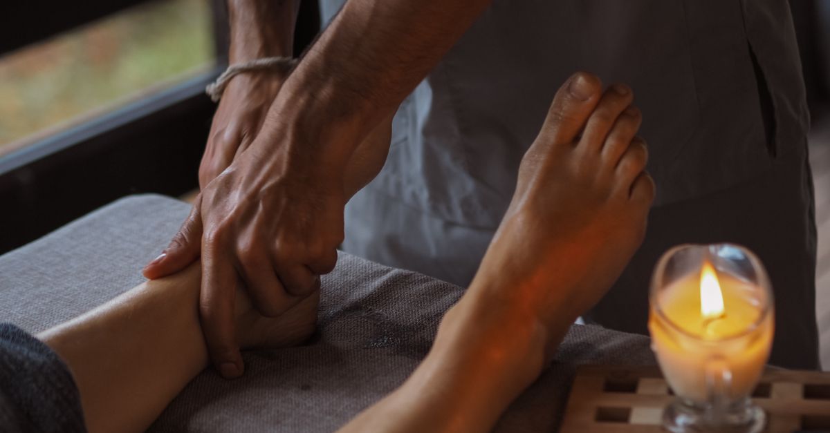 Close-up of a soothing foot massage in a dimly lit spa setting with a candle.