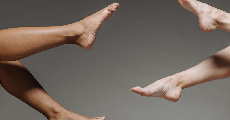 Artistic close-up of bare feet in diverse skin tones against a gray backdrop, studio setting.