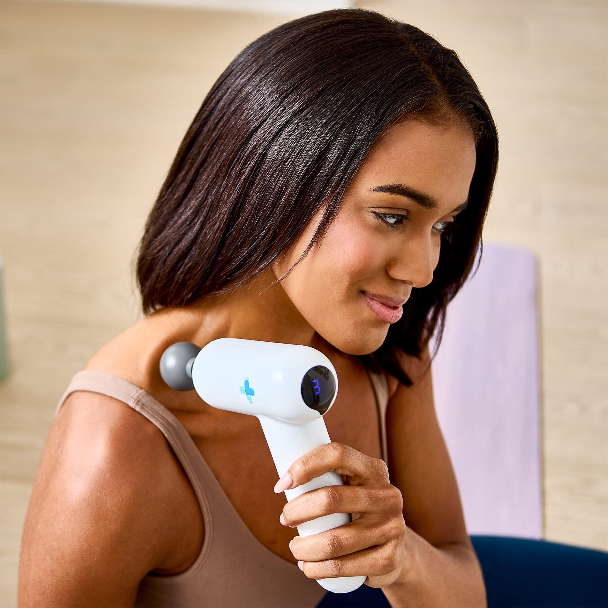 Woman holding Accuvibe Mini massager on shoulder indoors