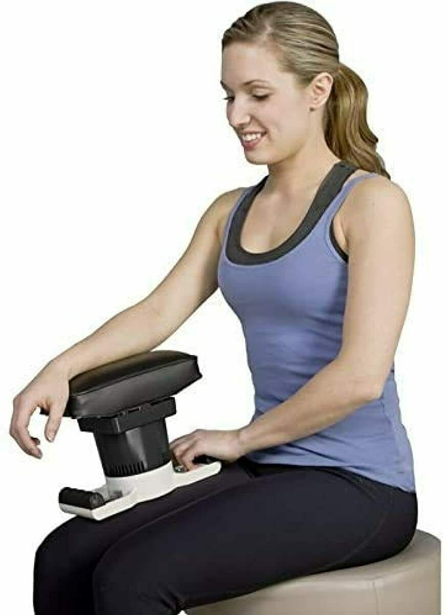 A woman in athletic wear sits on a stool, smiling as she uses the MedMassager MMB04 Body Massager, showcasing its effective pain relief benefits.